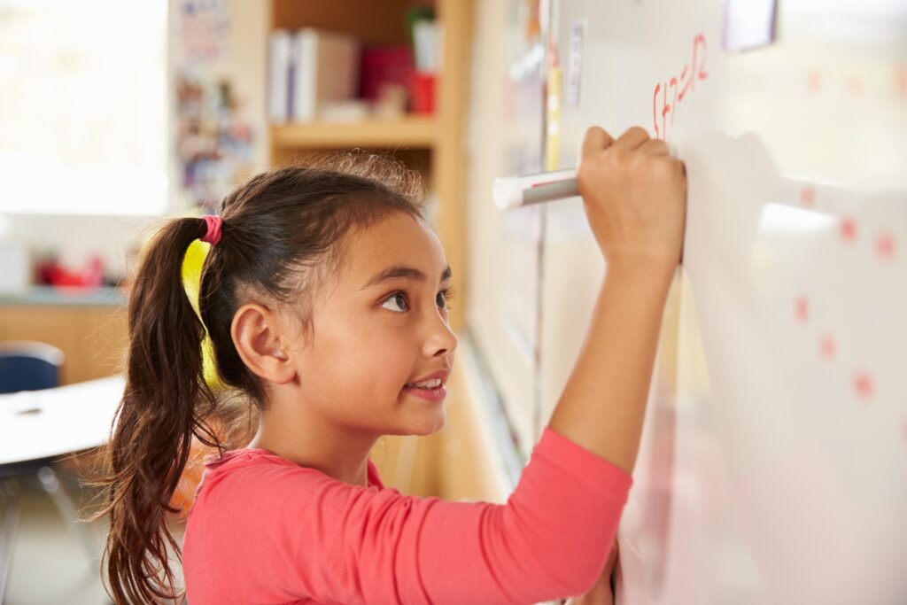 first grader girl doing math problems on whiteboard